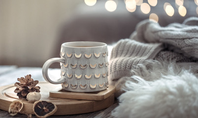 Coffee cup over Christmas lights bokeh in home on wooden table with sweater on a background and...