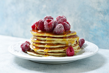 Stack of delicious homemade pancakes with maple syrup and fresh raspberry.