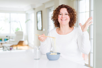 Senior woman eating asian noodles using chopsticks very happy and excited, winner expression celebrating victory screaming with big smile and raised hands