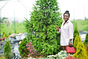 African woman in pink large shirt posed at garden with seedlings.