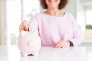 Close up of senior woman putting a coin inside piggy bank as savings smiling confident