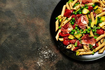 Penne pasta with grilled vegetables and prosciutto. Top view with copy space.