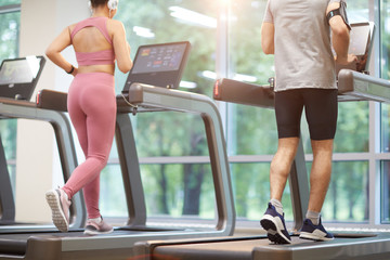 Fototapeta na wymiar Back view of two people running on treadmills in gym during cardio workout, copy space