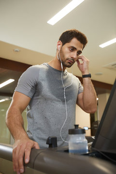 Waist Up Portrait Of Sweaty Young Man Listening To Music While Running On Treadmill In Gym