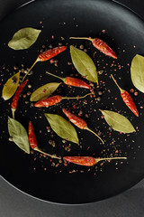 Red peppers and bay leafs on a black dish.