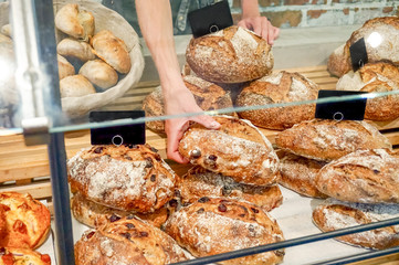 Loaves of bread at a bakery counter being sold and picked by a baker, behind a pane of glass. European artisan bread store, retail display.