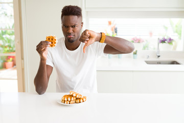 African american man eating sweet Belgian waffle with angry face, negative sign showing dislike...