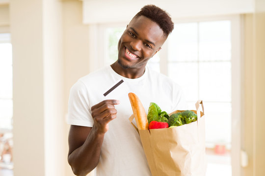 African american man holding paper bag full of groceries and holding credit card as payment