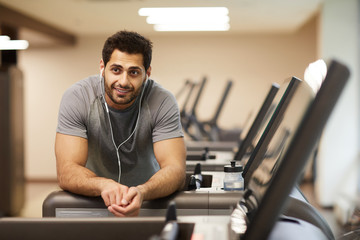 Portrait of muscular man taking break from workout in gym and listening to music, copy space