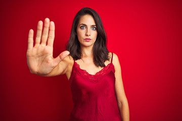 Young beautiful woman wearing sexy lingerie over red isolated background doing stop sing with palm of the hand. Warning expression with negative and serious gesture on the face.