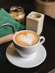 One cup of cappuccino with latte art on black table, white ceramic cup, top view. Cafe culture.