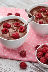 Two mugs of a hot chocolate with raspberries on a pink polka dots kitchen towel.