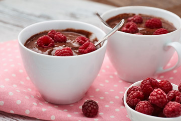 Two mugs of a hot chocolate with raspberries on a pink polka dots kitchen towel.