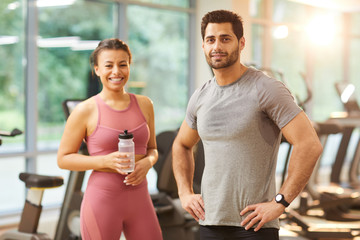 Waist up portrait of beautiful sportive couple looking at camera while posing in gym, copy space