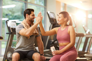 Portrait of beautiful sportive couple high five during workout in gym, copy space