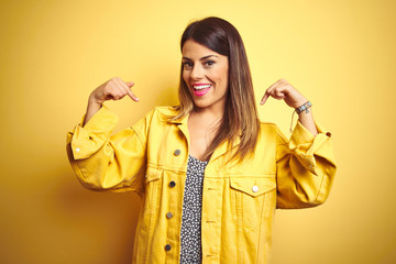 Young beautiful woman wearing denim jacket standing over yellow isolated background looking...