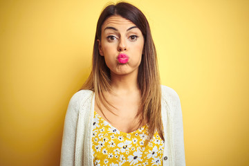 Young beautiful woman wearing jacket standing over yellow isolated background puffing cheeks with...