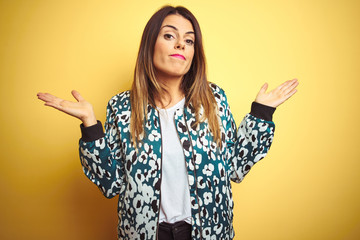 Young beautiful woman wearing casual jacket over yellow isolated background clueless and confused expression with arms and hands raised. Doubt concept.