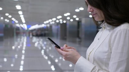 Passenger woman write to beloved using instant messaging application on smartphone, blurred empty airport passage seen on background. Lady stay with phone, type text using on-screen keyboard
