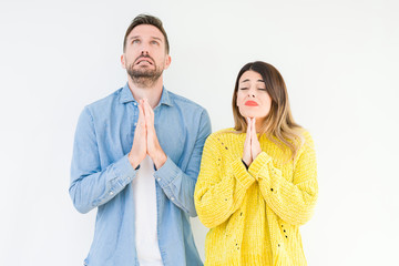 Young beautiful couple togheter over isolated background begging and praying with hands together with hope expression on face very emotional and worried. Asking for forgiveness. Religion concept.