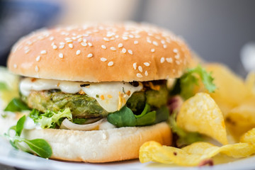 Hamburger vegetarian burger with green vegetables salad and cheese tofu cheese all vegan food with chips potato in blurred background