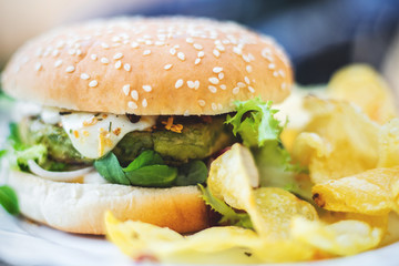 Hamburger vegetarian burger with green vegetables salad and cheese tofu cheese all vegan food with chips potato in blurred background