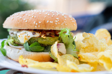 Hamburger vegetarian burger with green vegetables salad and cheese tofu cheese all vegan food with chips potato in blurred background