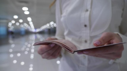 Woman stay and look to title page on international passport. Closeup shot of official document in passenger hands, blurred background.