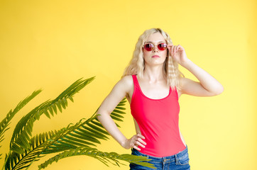 Portrait of beautiful blonde girl in sunglasses and red swimsuit against of yellow background