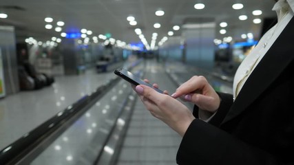 Lady type text on smartphone, stay on moving travolator at airport hall. Closeup shot of mobile device in woman hand, blurred background.