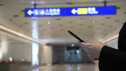 Passenger woman use smartphone at Chinese airport, closeup shot of hands holding mobile device, blurred background. Blue sign of international terminal navigation seen under ceiling
