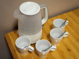 Fototapeta na wymiar White electric kettle and four white ceramic mugs with teaspoons on wooden table