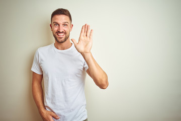 Young handsome man wearing casual white t-shirt over isolated background Waiving saying hello happy and smiling, friendly welcome gesture