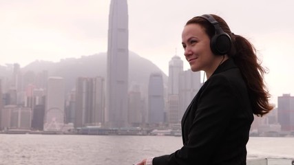 Lady listen music and enjoy Victoria Harbour panorama at cloudy day, half length side portrait, slow motion shot