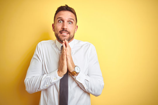 Young handsome business man wearing elegant white shirt over yellow isolated background praying with hands together asking for forgiveness smiling confident.