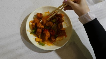 Woman pick up piece of pineapple from dish with sweet and sour meal, top-down shot. Lady have lunch at cheap Chinese eatery, using chopsticks to grab cuts from plate