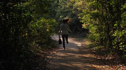 Tourist woman walk at rural path then run away, medium telephoto shot. Woman hurry to come back at nature trail, Lantau Island area. Lush dark green verdure surround pedestrian pathway