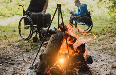 Disabled man resting in a campsite with friends. Wheelchair in the forest on the background of...