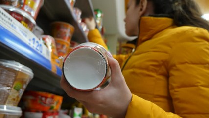 Female customer choose quick noodles at grocery store, hold one cup in hand in front of camera and look to other products, low angle shot. Woman pick up other type from shelf and look around package
