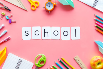 Education concept with school word and frame of stationery with notebook, pens, clock on pink background top view