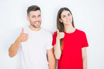 Young beautiful couple together over white isolated background doing happy thumbs up gesture with hand. Approving expression looking at the camera with showing success.