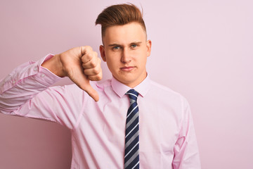 Young handsome businessman wearing shirt and tie standing over isolated pink background looking unhappy and angry showing rejection and negative with thumbs down gesture. Bad expression.