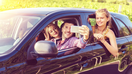 Happy best friends having fun together taking selfie while traveling by car on road trip adventure