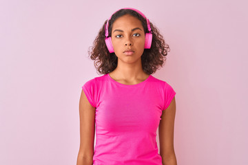 Obraz na płótnie Canvas Young brazilian woman listening to music using headphones over isolated pink background with a confident expression on smart face thinking serious