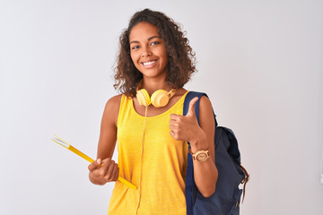 Brazilian student woman wearing backpack holding notebook over isolated white background happy with big smile doing ok sign, thumb up with fingers, excellent sign