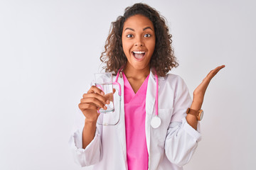 Young brazilian doctor woman holding glass of water standing over isolated white background very happy and excited, winner expression celebrating victory screaming with big smile and raised hands