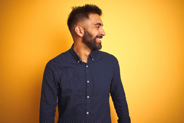 Young handsome indian businessman wearing shirt over isolated yellow background looking away to side with smile on face, natural expression. Laughing confident.