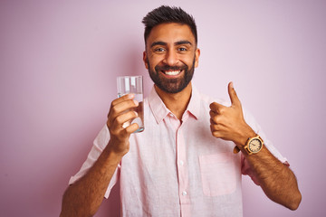 Young handsome indian man dinking glass of water over isolated pink background happy with big smile...