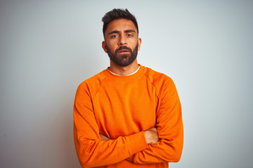 Fototapeta premium Young indian man wearing orange sweater over isolated white background skeptic and nervous, disapproving expression on face with crossed arms. Negative person.