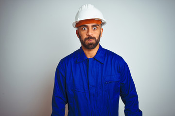 Handsome indian worker man wearing uniform and helmet over isolated white background puffing cheeks with funny face. Mouth inflated with air, crazy expression.